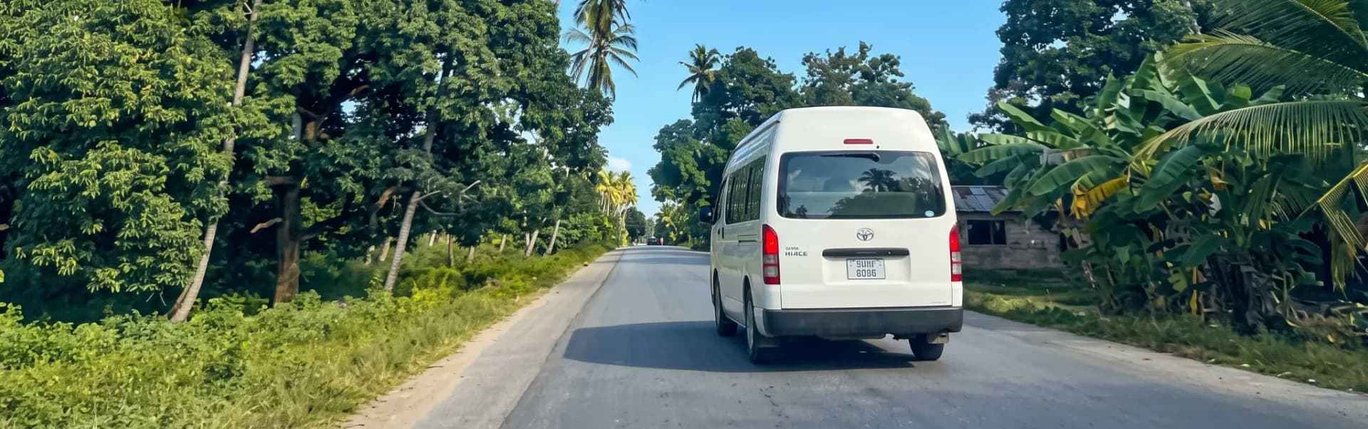 Un minivan bianco della navetta condivisa su una strada fiancheggiata da palme a Zanzibar